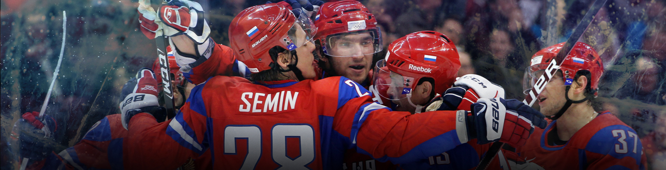 Хоккеисты в красной форме с российскими флагами на шлемах обнимаются, празднуя победу или забитый гол. Видны номера и фамилии на форме. Настроение радостное, игроки собраны в центре кадра